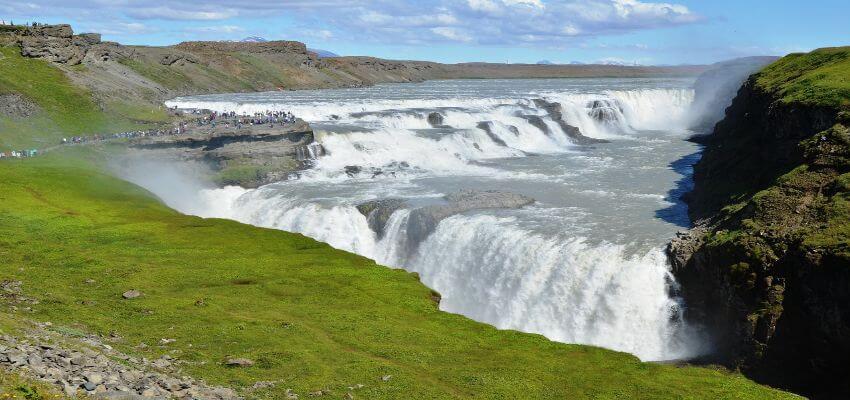 Ein mächtiger und breiter Wasserfall umgeben von einer grünen Moos bedeckten Umgebung.