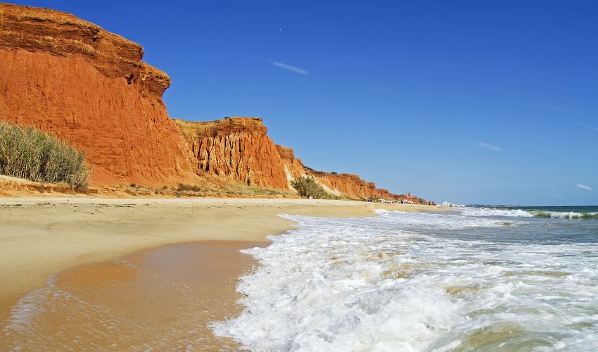 Sandstrand mit Klippen aus rotem Sandstein im Hintergrund.