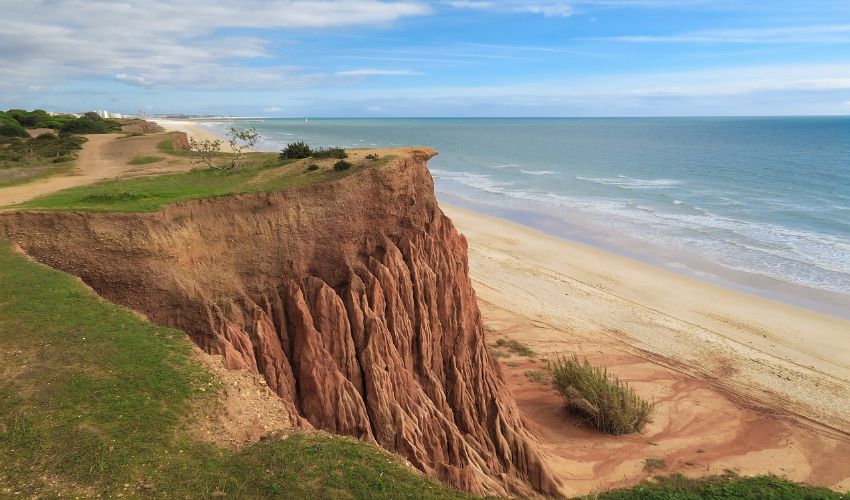 Sandstrand mit roter Klippenwand im Hintergrund.