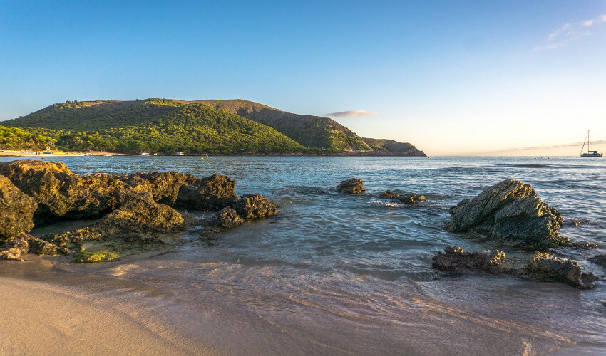 Ein einsamer Strand mit großen Felsen im seichten Wasser.