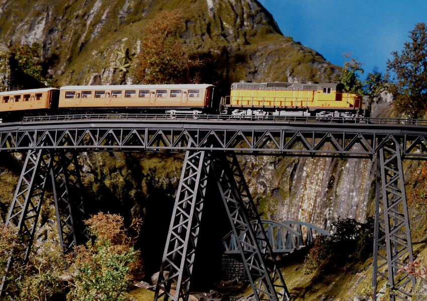 Eine gelbe Eisenbahn fährt auf einer hohen Metallbrücke.