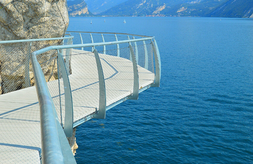 Ein Steg, der an einer Klippe entlang geht. Direkt darunter der Gardasee.