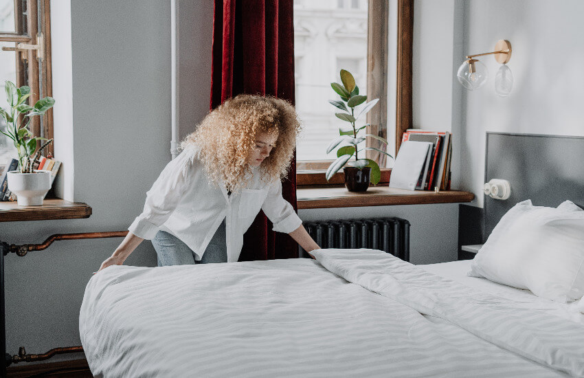 Eine Frau bezieht ein Bett mit weißen Lacken.
