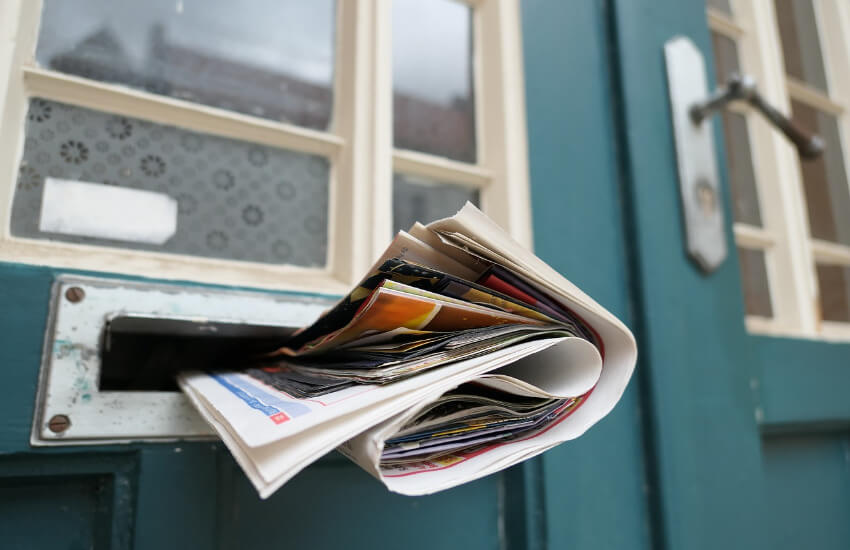 Ein in eine Holztür eingebauter Briefkasten, welcher voll mit Zeitungen ist.