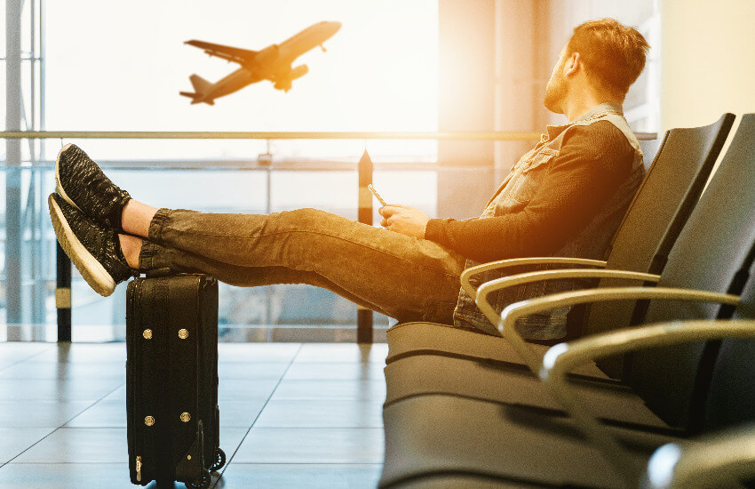 Ein Mann sitzt im Wartebereich eines Flughafens und sieht einem Flugzeug beim Start zu.