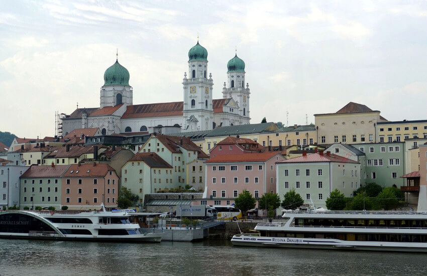 Zwei Flusskreuzfahrtschiffe auf der Donau, die in Passau ankern, dahinter der Dom St. Stephan.