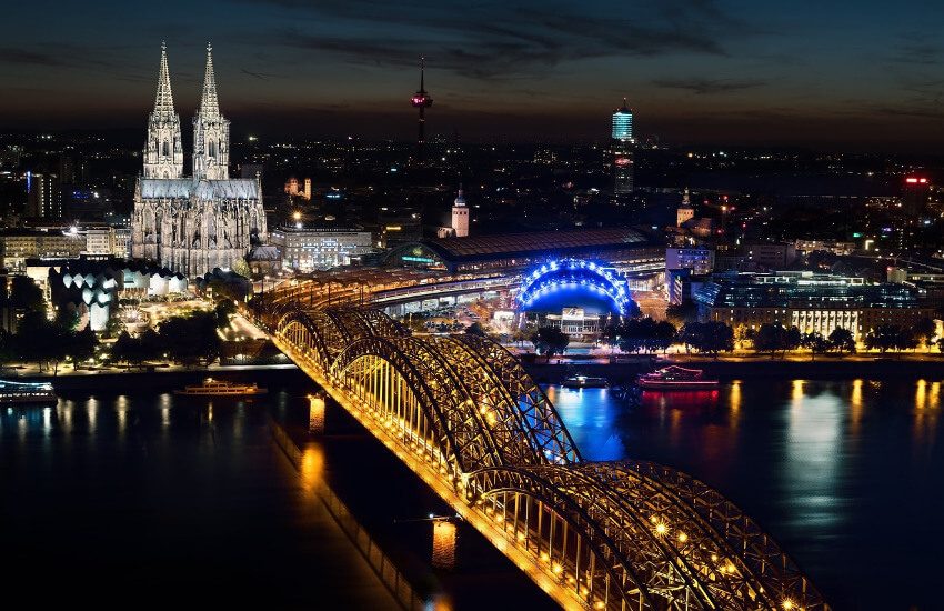 Die Hohenzollernbrücke und der Kölner Dom beleuchtet in der Dunkelheit.