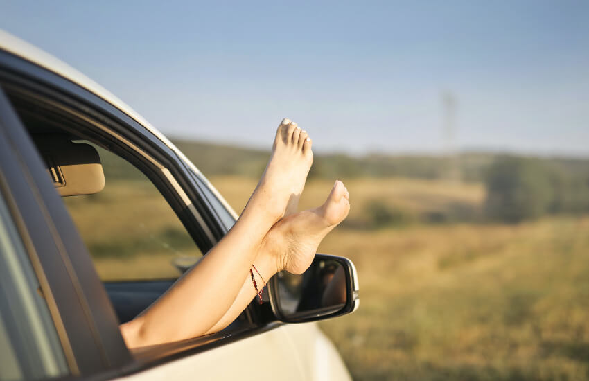 Eine Frau streckt Ihre Füße beim Autofenster hinaus.