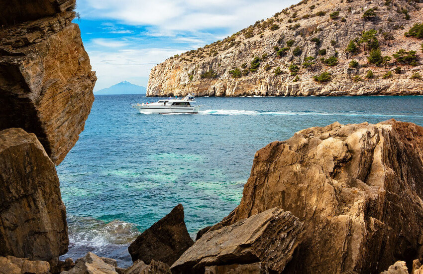 Eine Bucht mit steilen Felsklippen und dazwischen am Meer fährt eine Yacht.