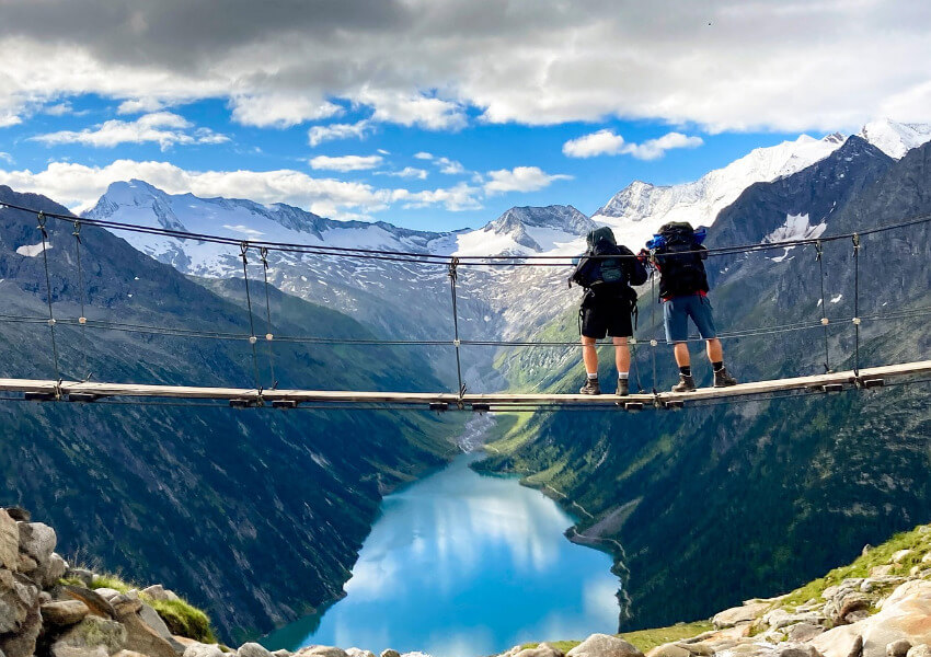 Panorama-Blick auf den türkisfarbenen Schlegeis-Stausee im Zillertal, eingerahmt von den schneebedeckten Gipfeln der Zillertaler Alpen unter strahlend blauem Himmel.